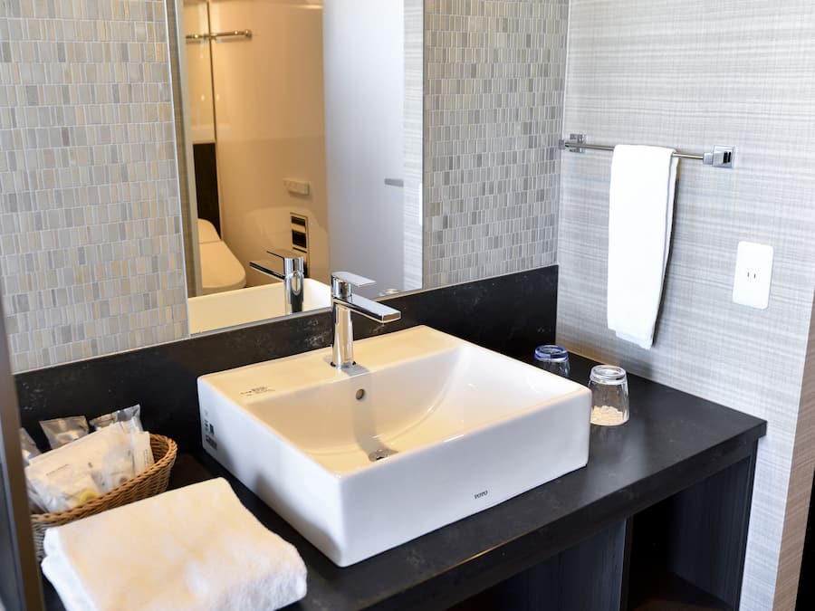 A modern bathroom with a white sink, a mirror, and a towel rack.