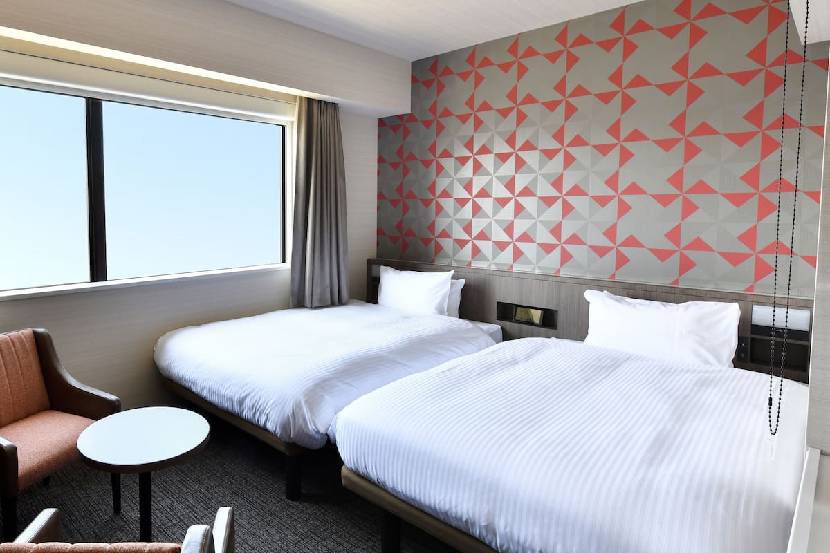 A hotel room with two beds, a small round table, a sofa, and a desk.