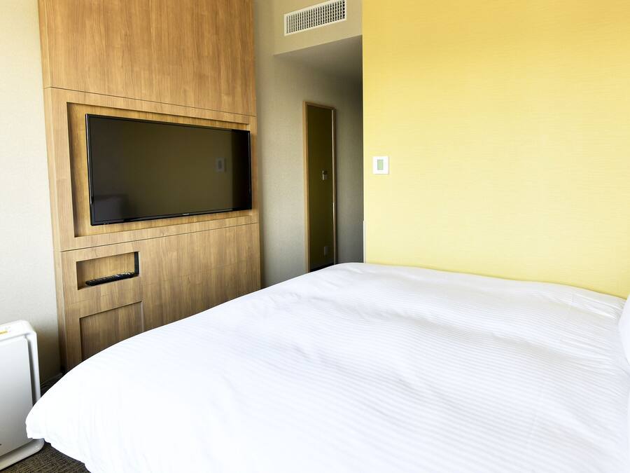 A hotel room with a bed, a TV mounted on a wooden cabinet, and a small heater.