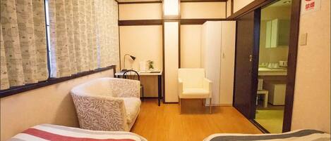 A hotel room with two beds, a desk, a chair, and a sliding door leading to a bathroom.