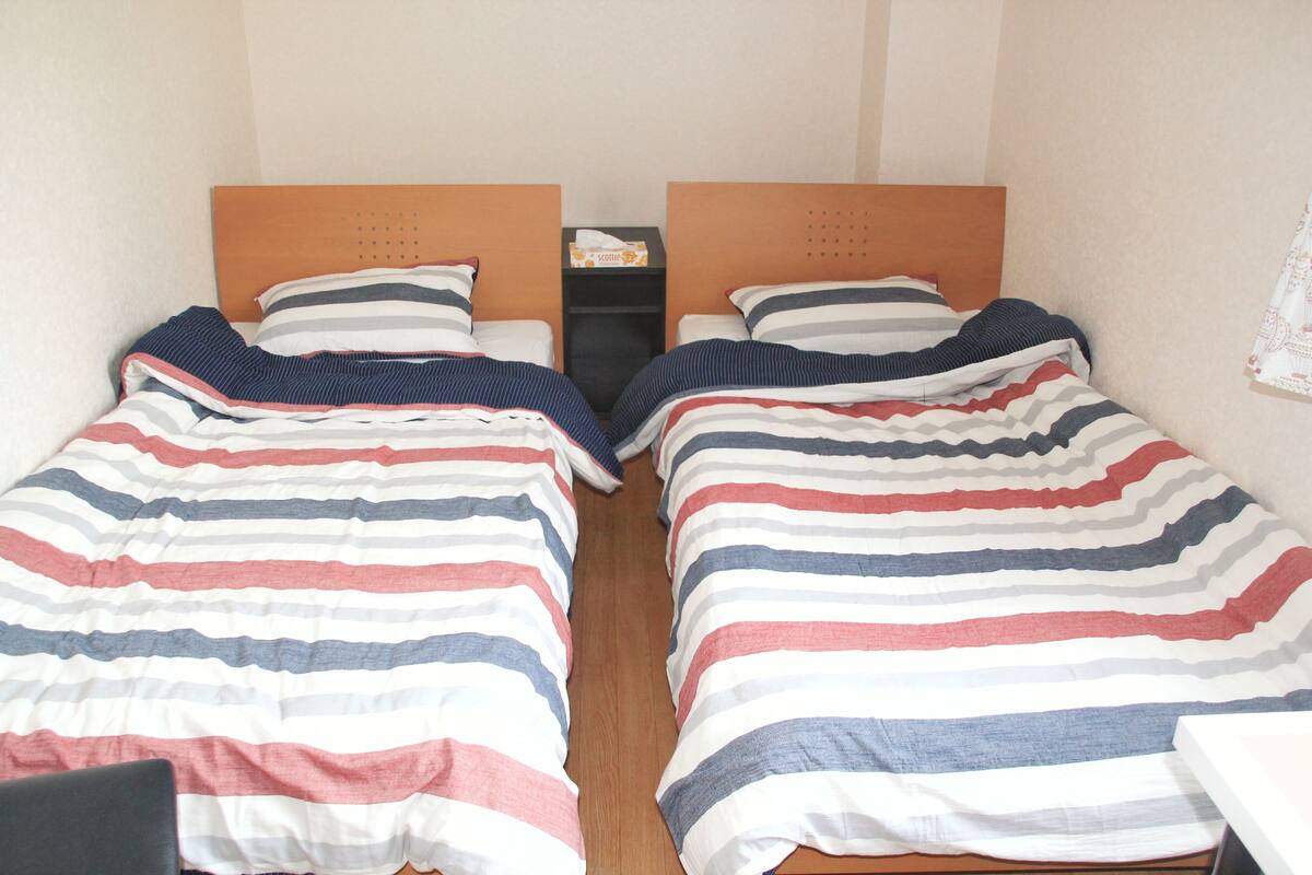 A double room with two beds, each with striped bedding, a wooden headboard, and a nightstand between them.