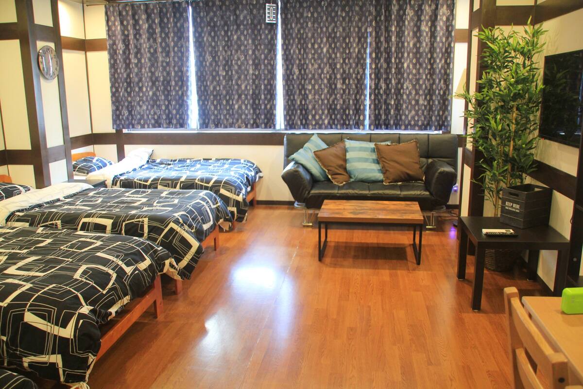 A room with two beds, a sofa, a wooden coffee table, a TV, and a plant.