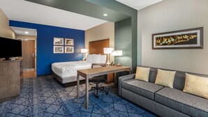 A hotel room with a bed, a desk with a chair, a sofa, a TV, and framed pictures on the wall.