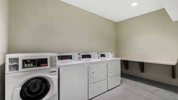A laundry room with a front-loading washer and dryer, a shelf above the dryer, and a tiled floor.