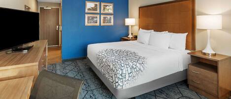 Habitación de hotel con una cama grande, un escritorio con televisor de pantalla plana, dos lámparas de noche y una pared con cuatro cuadros.