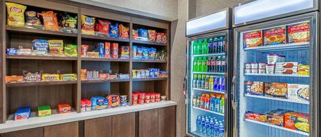 Un área de exhibición de bocadillos y bebidas, con estantes llenos de diferentes opciones y una sección refrigerada para bebidas.