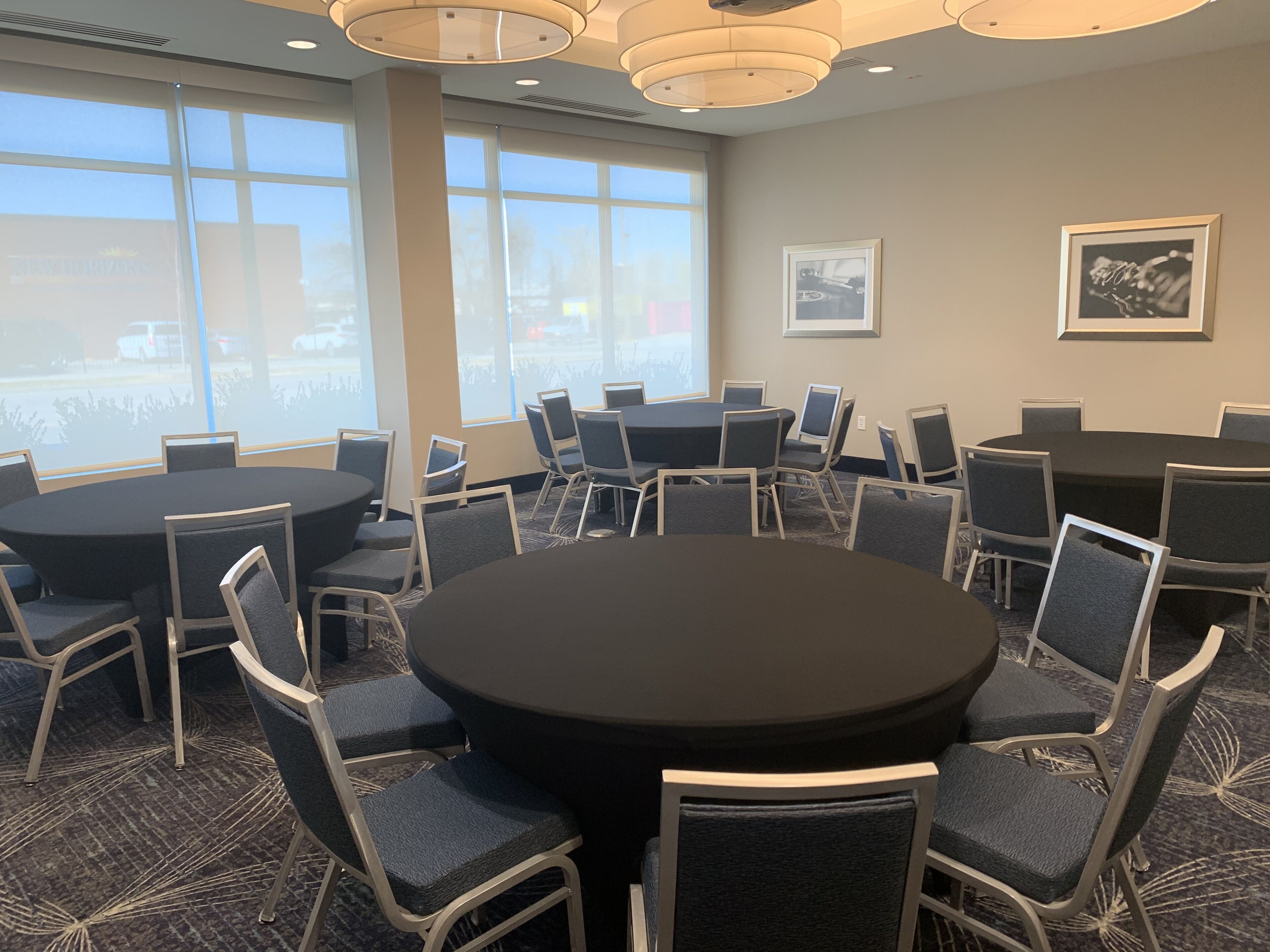 A conference room with round tables and chairs, large windows, and framed pictures on the walls.