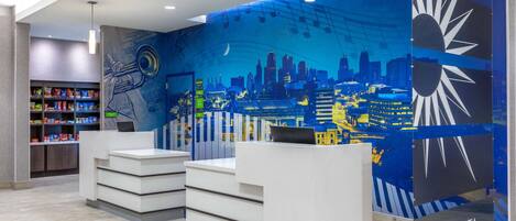A hotel reception area with a cityscape mural, a reception desk, and a shelf with snacks.