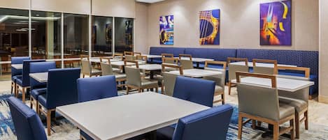 Uma área de refeições de hotel com mesas e cadeiras, obras de arte nas paredes e um chão coberto de carpete.