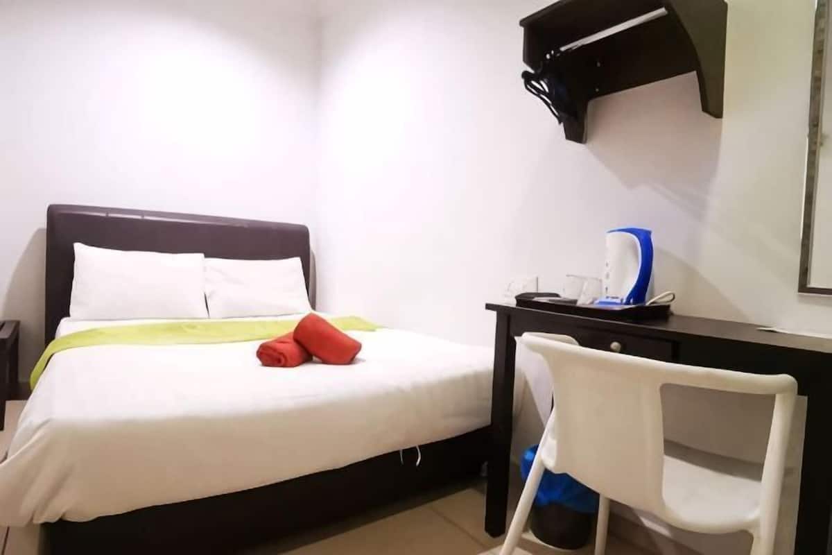 Quarto de hotel com cama, escrivaninha com cadeira, cafeteira e uma mesa pequena.