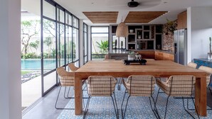 Uma sala de jantar espaçosa com uma grande mesa de madeira e cadeiras de vime, com vista para uma piscina.