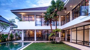Uma casa moderna de dois andares, com piscina, grandes janelas e um gramado bem cuidado.