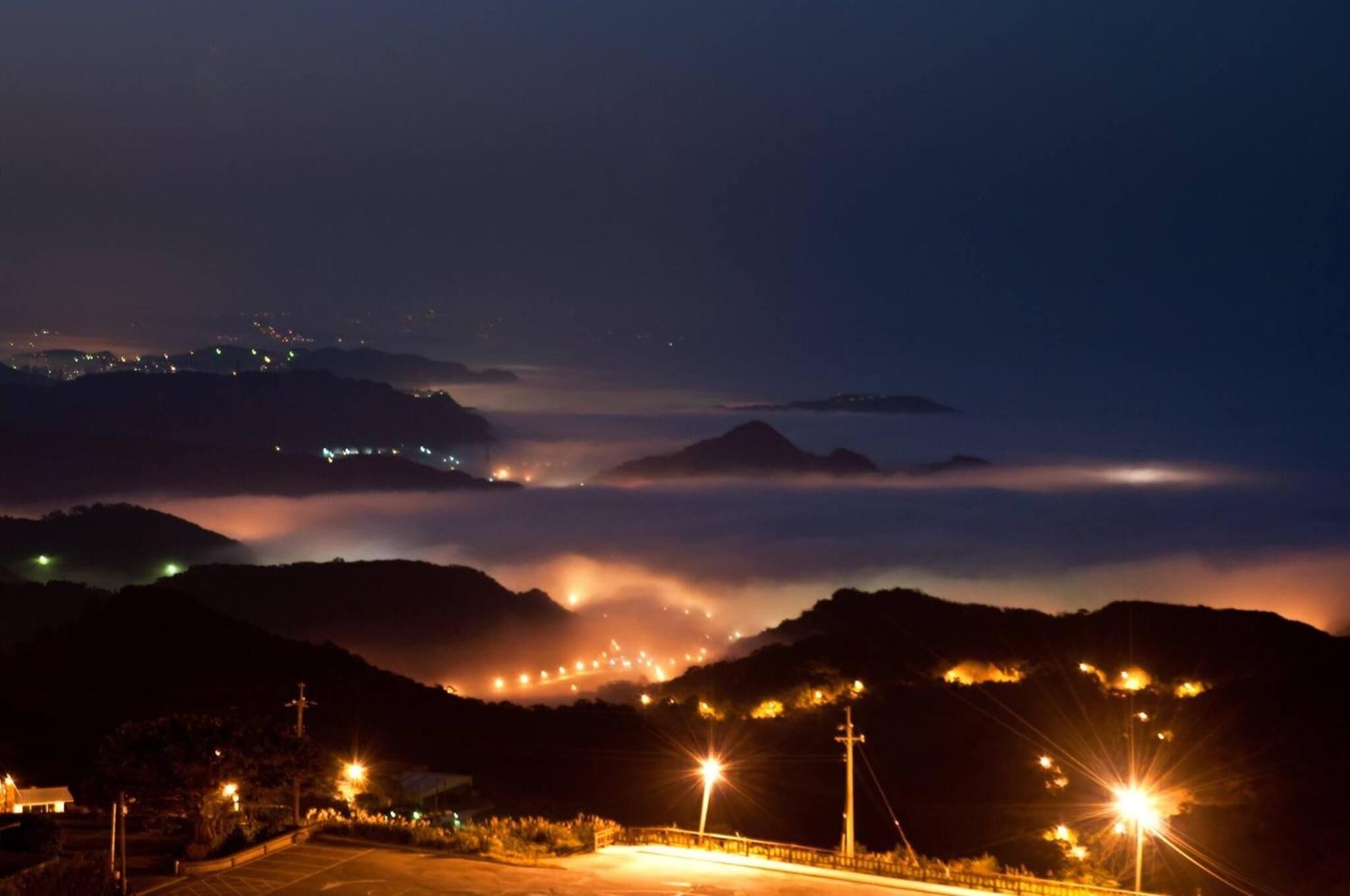 A nighttime view of a mountainous area with streetlights and distant city lights.