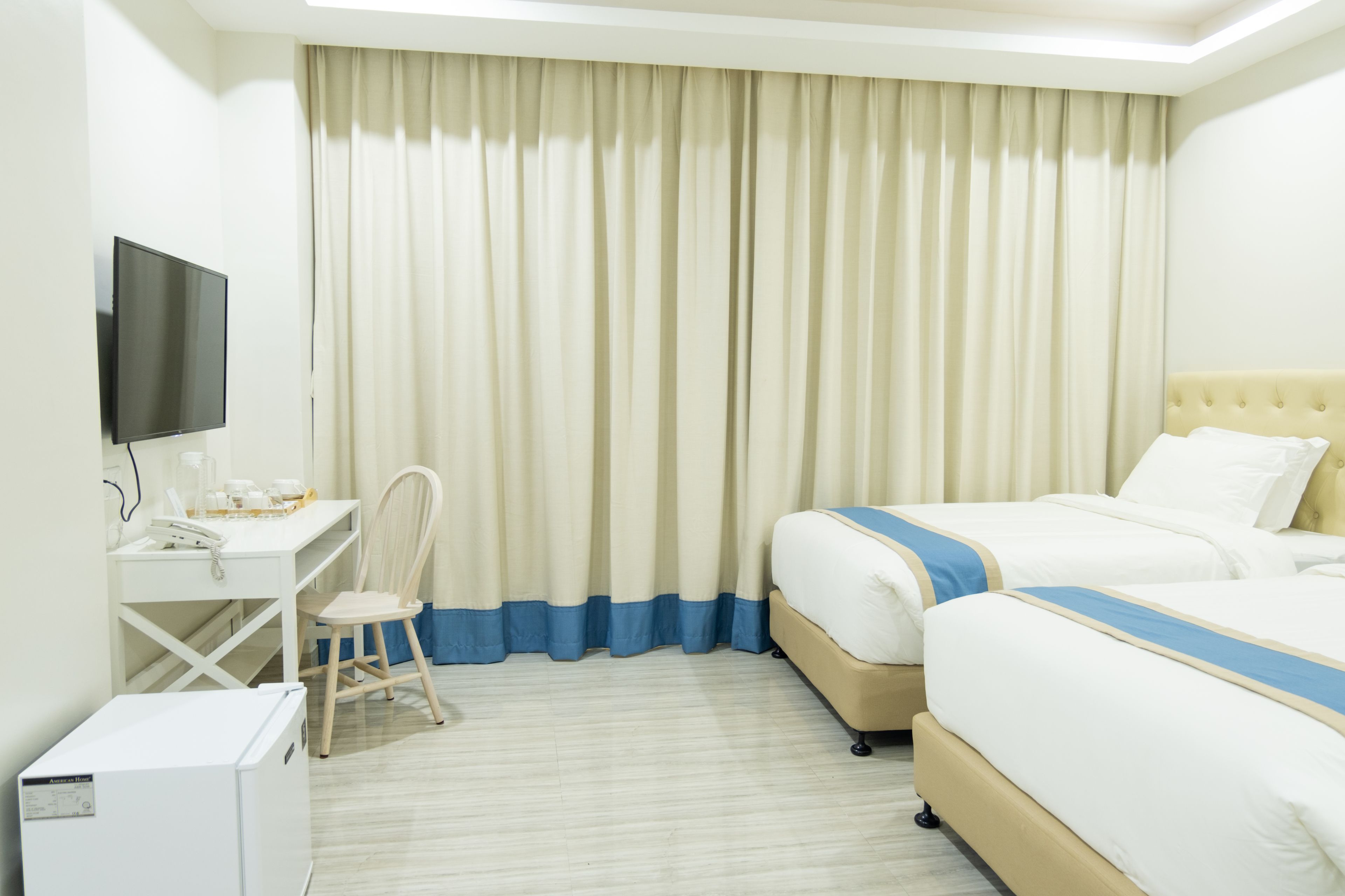 A hotel room with a bed, a desk with a chair, a television, and a refrigerator.