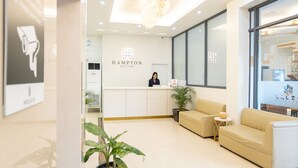 Un espace d’accueil comprenant un comptoir de réception, une réceptionniste, un canapé, une plante en pot et un lustre.