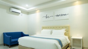 Une chambre d’hôtel moderne avec un grand lit, un fauteuil bleu, une table de chevet et un climatiseur fixé au mur.