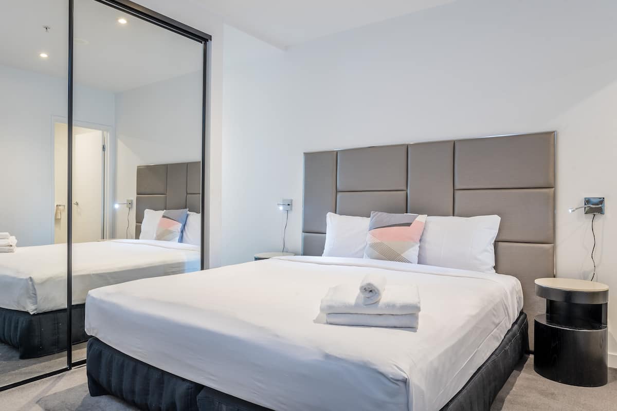 Ein modernes Hotelzimmer mit zwei Betten, einem großen Spiegel und einem runden Beistelltisch.