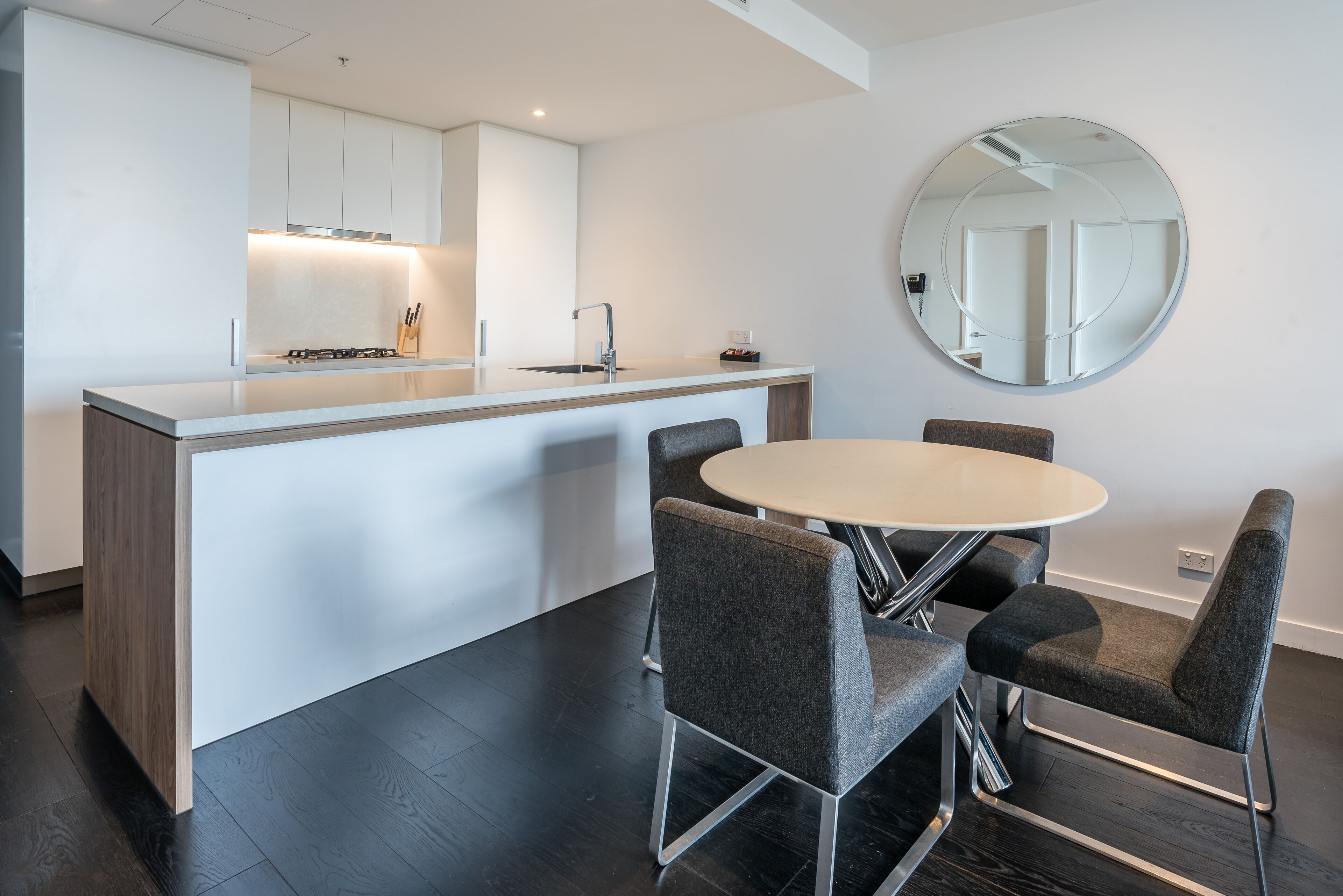 Une cuisine moderne avec un îlot central, une table à manger ronde et quatre chaises grises.