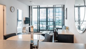 A modern hotel room with a large window, a round table, and a built-in sink. - FV By Serain Residences (Fortitude Valley)