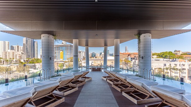 An infinity pool with wooden loungers and a city view. - FV By Serain Residences (Fortitude Valley)