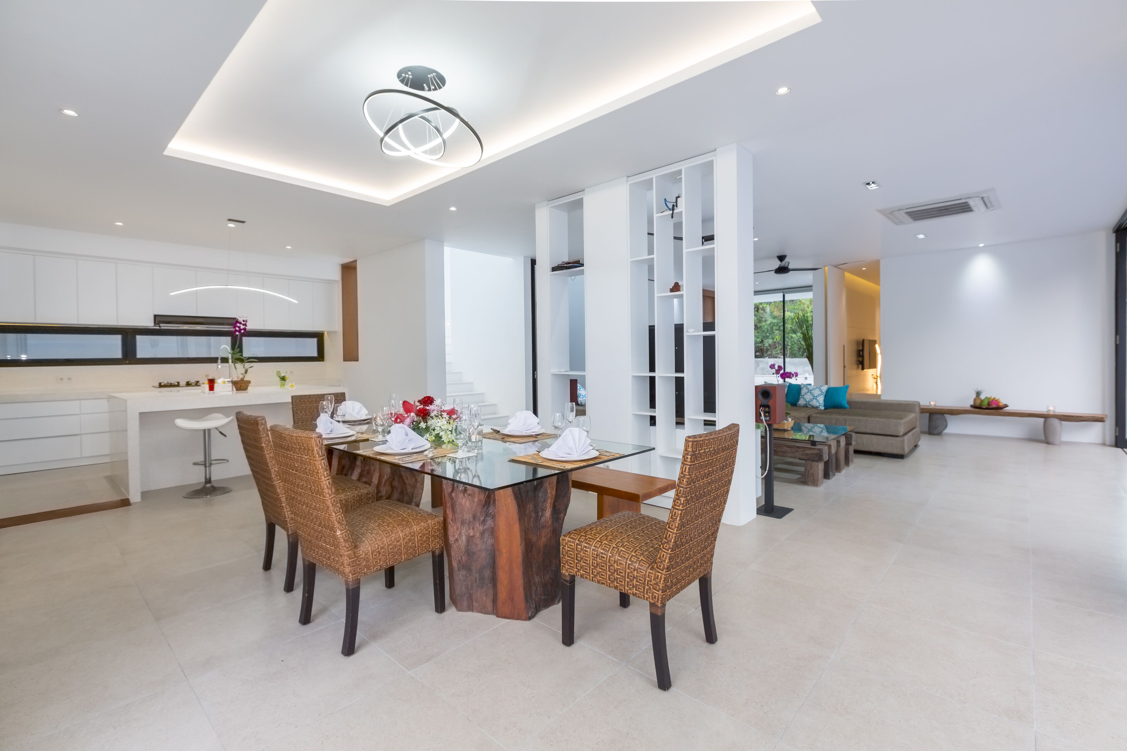 A modern kitchen with white cabinetry, a dining area with a glass table and wicker chairs, and a living area with a sofa and a coffee table.