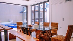A modern dining area with a glass-top table, wooden benches, and patterned chairs. - Villa Damar Canggu by Nagisa Bali (Canggu)