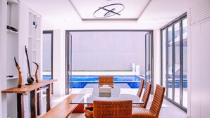 A modern dining area with a glass table and wicker chairs, overlooking a pool. - Villa Damar Canggu by Nagisa Bali (Canggu)