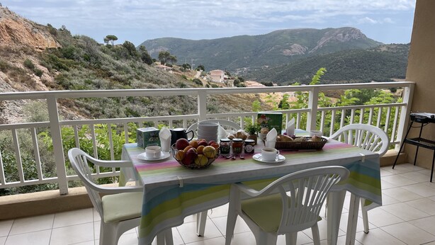 Ein Balkon mit Frühstückstisch, weißen Stühlen und Blick auf Hügel.