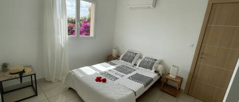Une chambre à coucher comprenant un lit, une table de chevet, une commode, une fenêtre avec des rideaux et un appareil de climatisation.