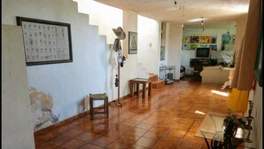 Un amplio salón con suelo de baldosas, una escalera y un televisor al fondo.