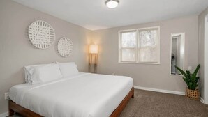A bedroom with a bed, two wall-mounted circular decorations, a bedside lamp, a window with blinds, and a potted plant. - Charming Home | Near Spokane City Center (Spokane)