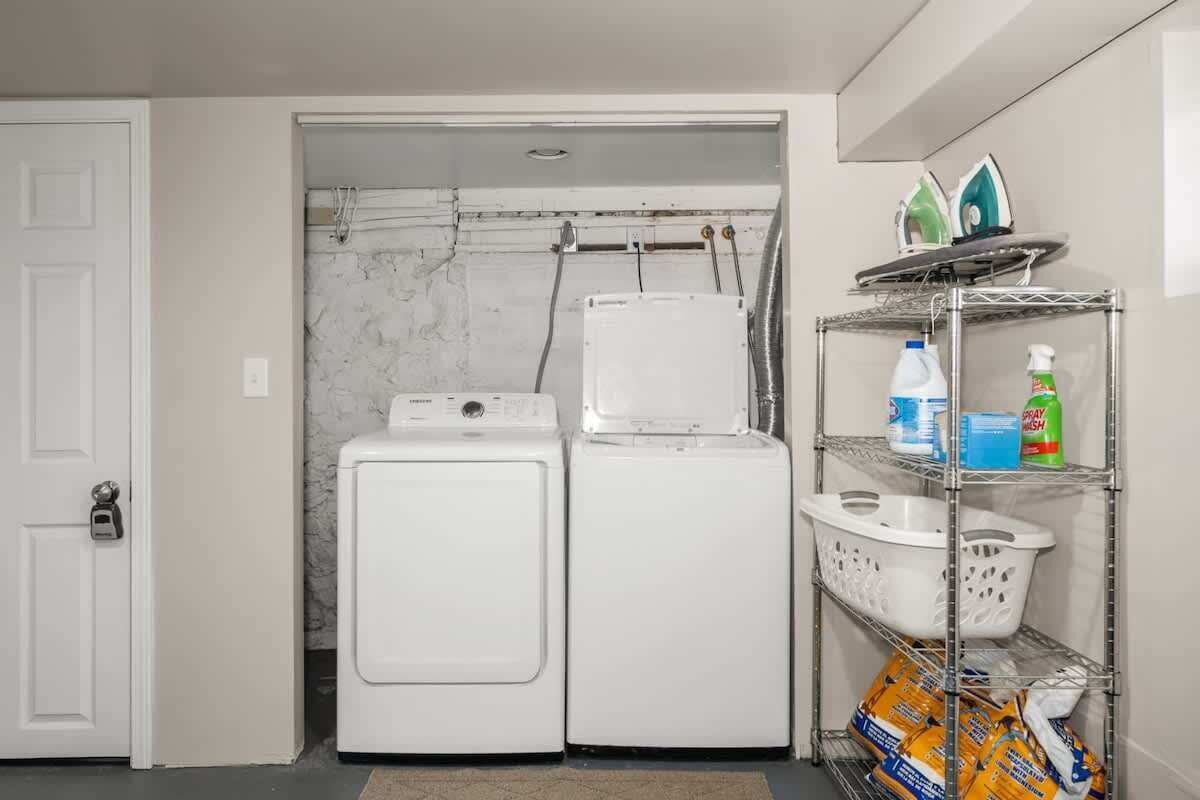 Une buanderie équipée de deux machines à laver blanches, d’une étagère contenant des produits de nettoyage et d’une porte dotée d’un dispositif de sécurité.