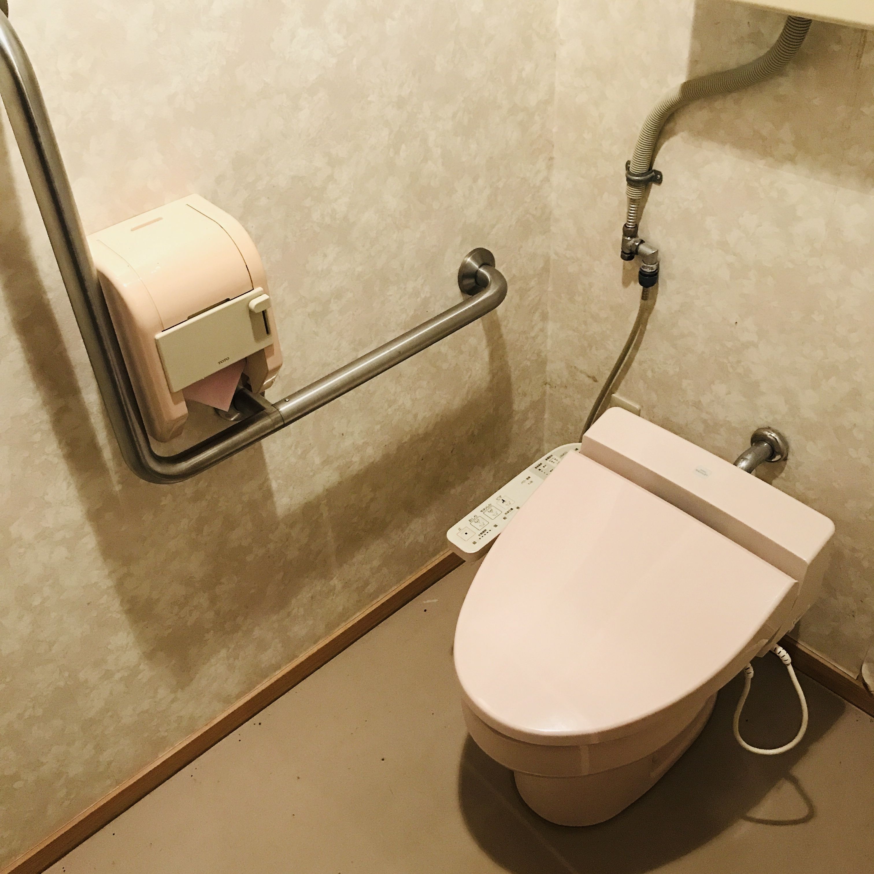 A toilet with a paper towel dispenser and a handrail.