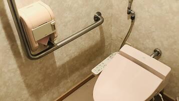 A toilet with a paper towel dispenser and a handrail.