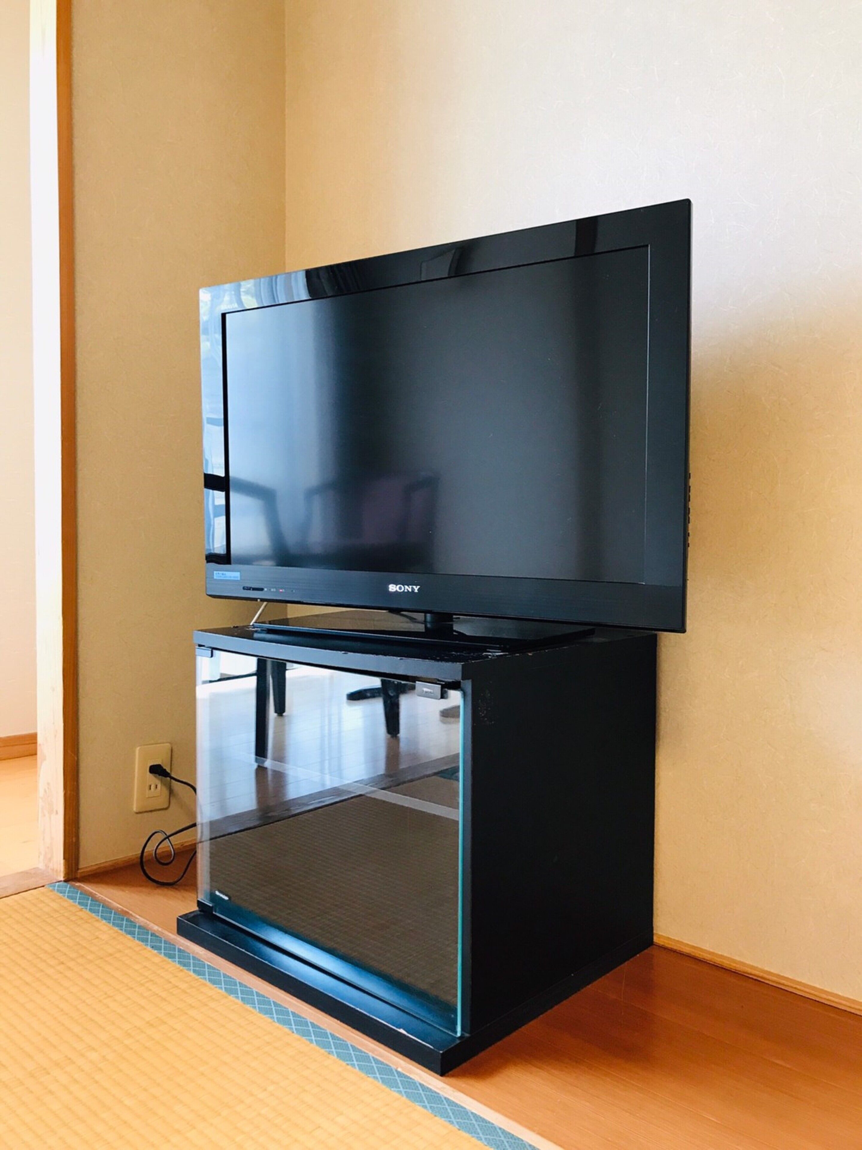 A black Sony TV on a stand in a room with wooden flooring and a plain wall.