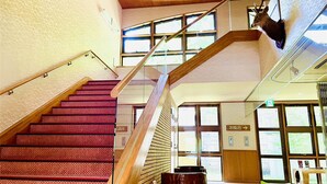 A staircase with red carpeted steps, wooden handrails, and large windows allowing natural light. - Lake Side Nikko Hotel (Nikko)