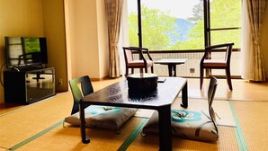 A room with a dining table, chairs, a television, and a large window with curtains. - Lake Side Nikko Hotel (Nikko)