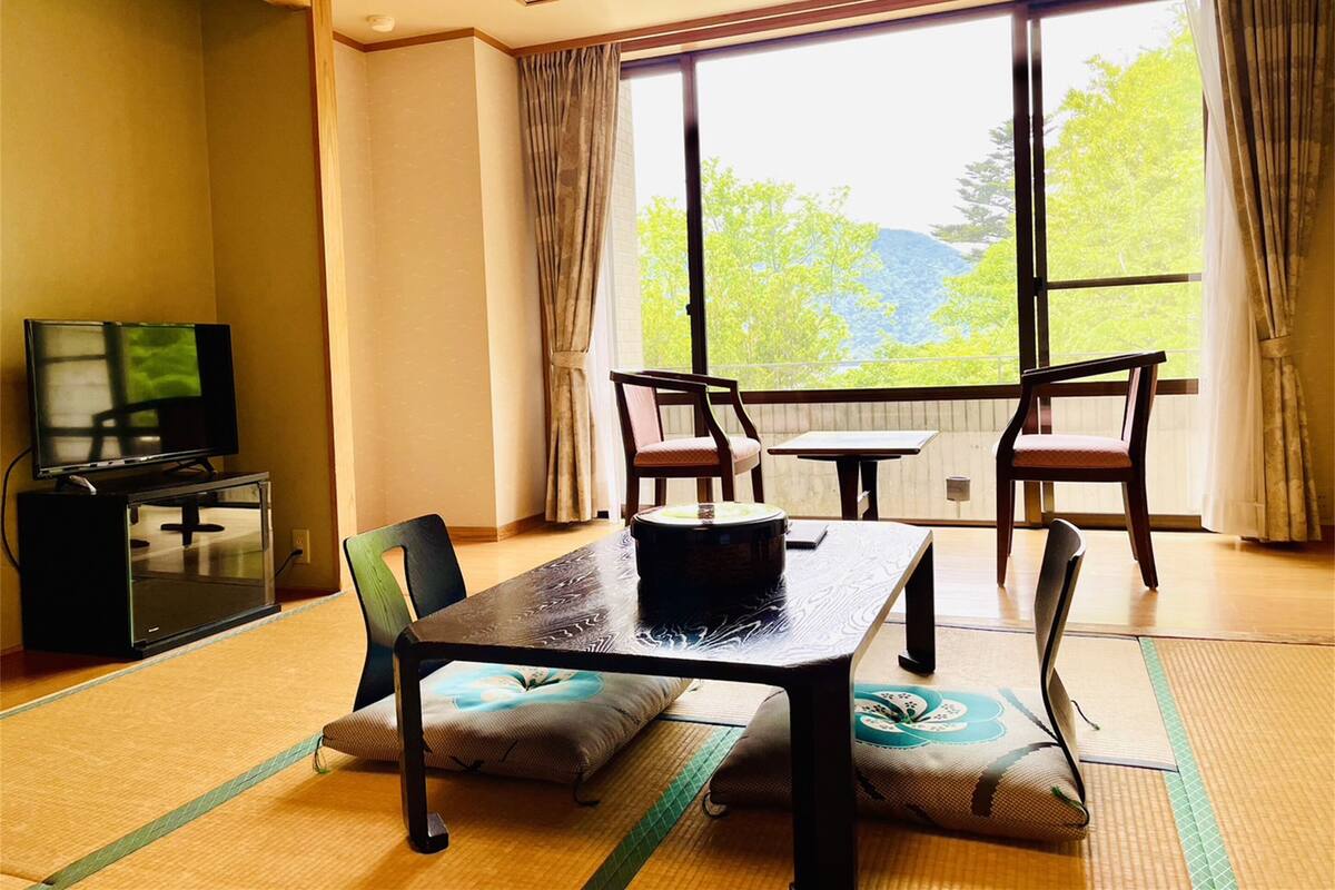 A room with a dining table, chairs, a television, and a large window with curtains.