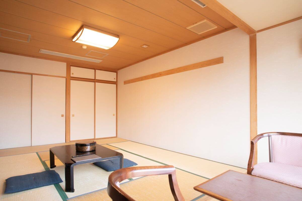 A traditional Japanese room with tatami flooring, a low table with a bowl, a cushioned chair, and sliding doors.