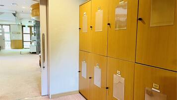 Una fila de taquillas de madera con etiquetas numeradas, suelo alfombrado y una puerta que da a una habitación con equipo médico.