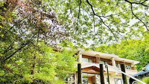 A modern two-story building with a wooden facade, surrounded by lush greenery and trees. - Lake Side Nikko Hotel (Nikko)