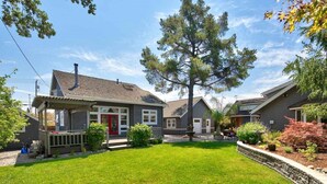A residential property with a well-maintained lawn, a large tree, and a house with a red door and a porch.