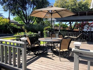 Relax on the patio with a round table and four chairs, surrounded by lush greenery and a shaded area.