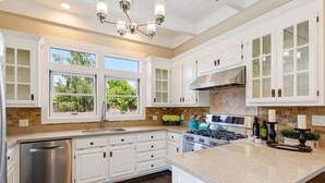A modern kitchen with white cabinetry, a stainless steel dishwasher, a gas stove, and a large island with a granite countertop.
