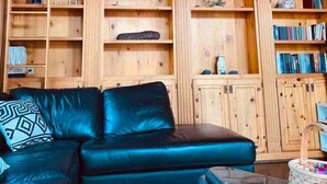 A living room with a black leather sofa, wooden shelving with various decorative items, and a glass coffee table.