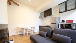 Ein modernes Wohnzimmer mit einer Couch, einem Esstisch mit Stühlen und einer Küchenzeile inklusive Mikrowelle und Kaffeemaschine.