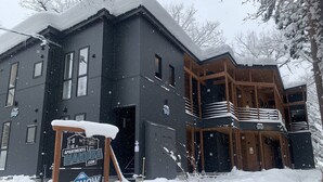 Ein zweistöckiges Gebäude mit dunkler Fassade, mehreren Fenstern und einem Balkon mit Geländer.