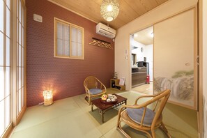 A traditional Japanese room with tatami flooring, a low table with a decorative item, two tatami chairs, a hanging clothes rack, and a sliding door leading to another room.