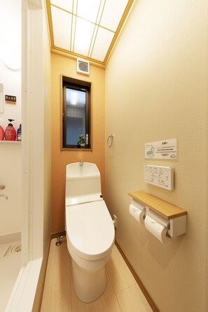A compact bathroom with a toilet, a small window, and a wall-mounted toilet paper holder.