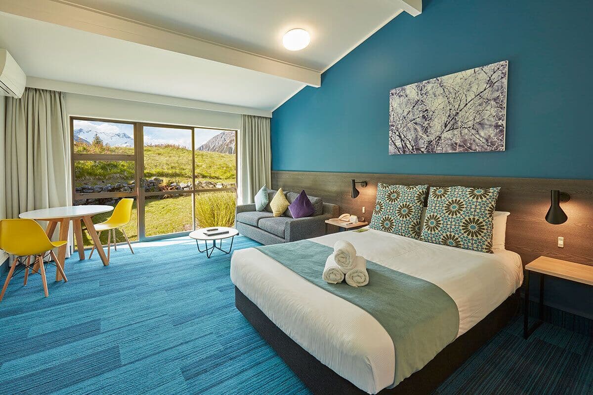 A hotel room with a large bed, a sofa, a dining table, and a view of the outdoors.